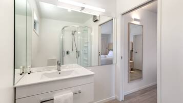 Un baño moderno con un espejo grande, cabina de ducha de vidrio y tocador blanco con lavamanos y toallero.