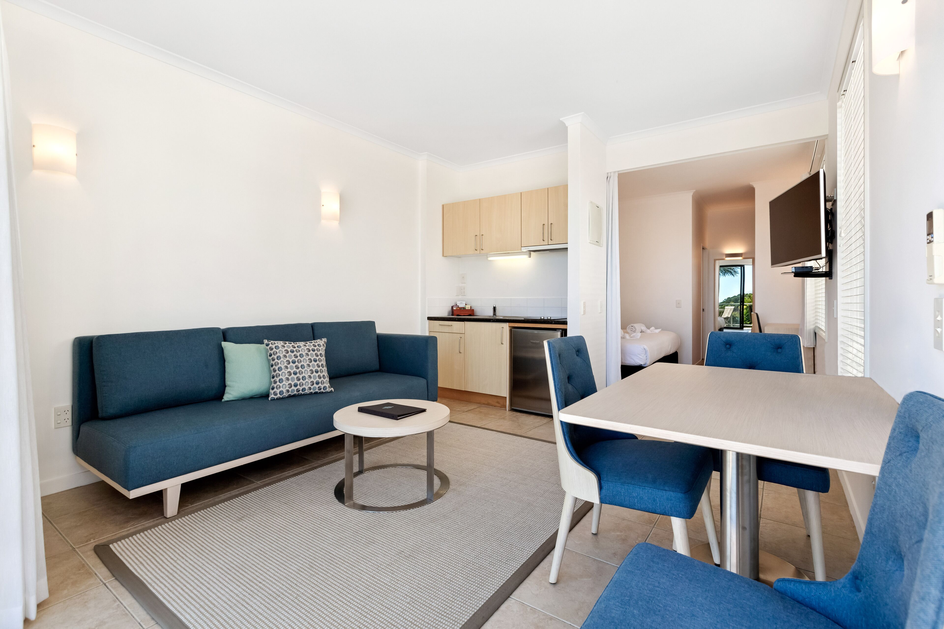 Een moderne woonkamer met een blauwe bank, een ronde salontafel en een eethoek met een witte tafel en blauwe stoelen.