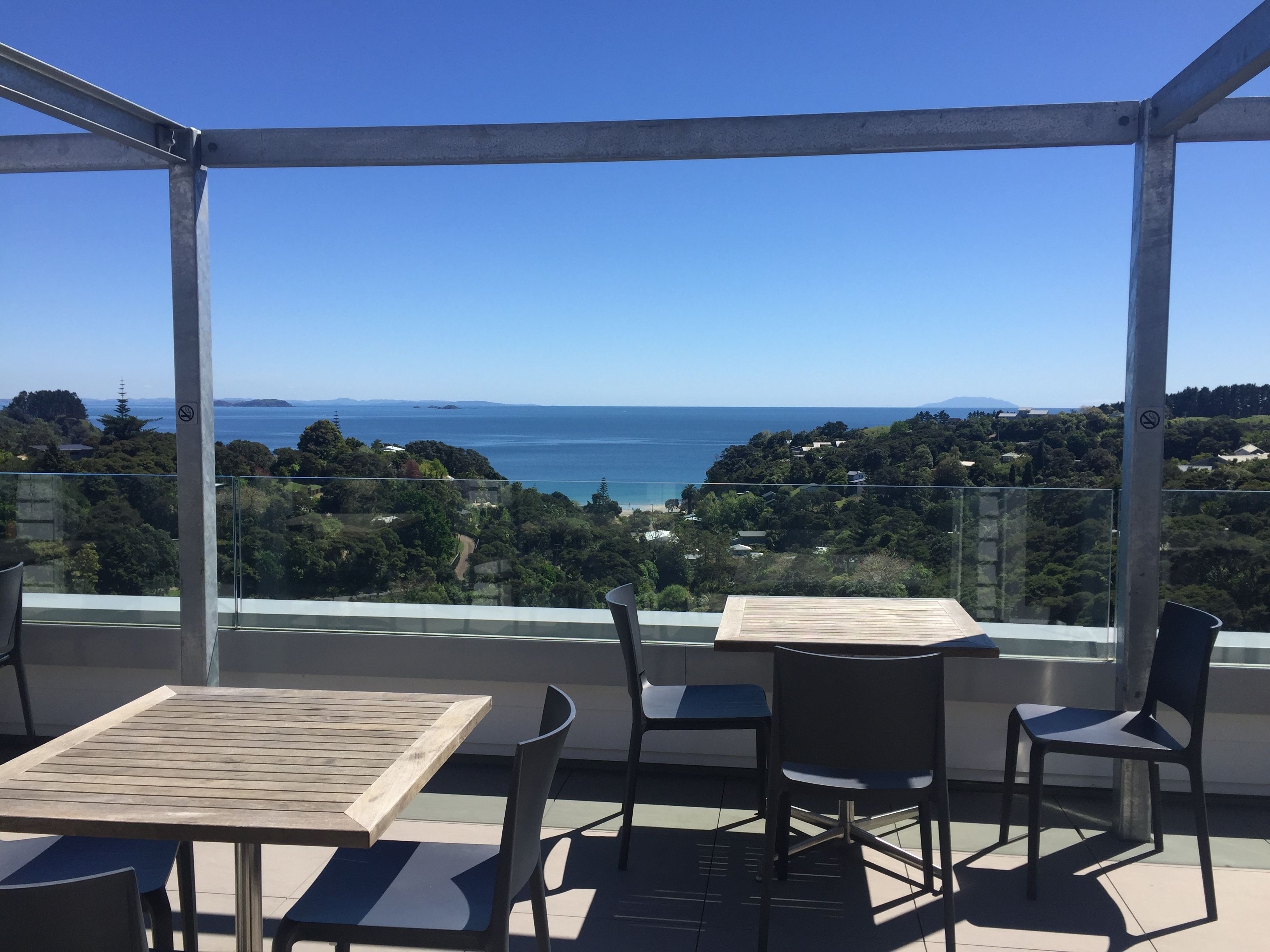A balcony with a table and chairs, overlooking a coastal landscape with trees and a view of the sea.