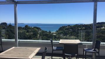 Ein Balkon mit Tisch und Stühlen, der auf eine Küstenlandschaft mit Bäumen und Meerblick blickt.