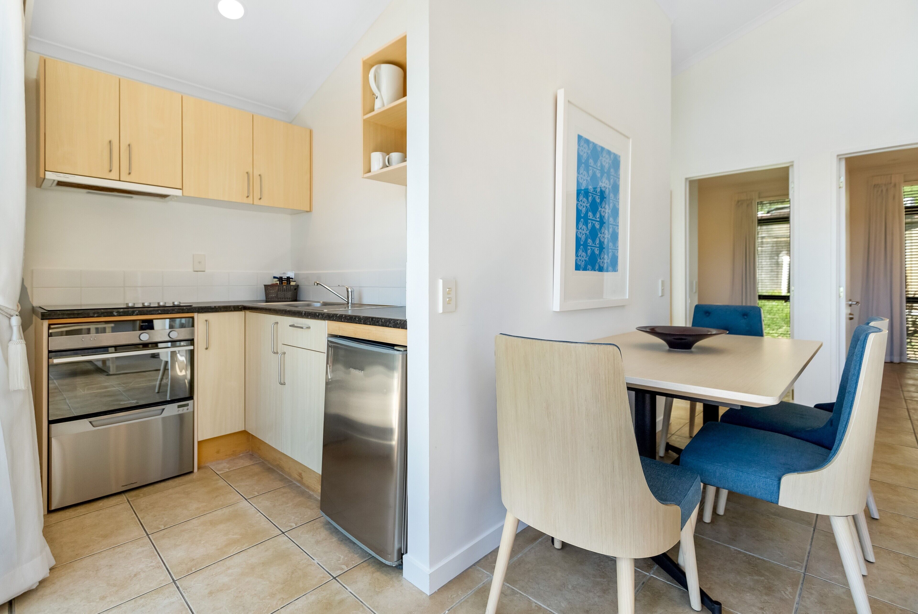 A compact kitchen with built-in appliances, a dining area with a table and chairs, and a framed artwork on the wall.