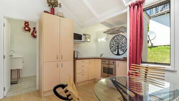 A modern kitchen with a glass dining table, wooden cabinets, and a red curtain.
