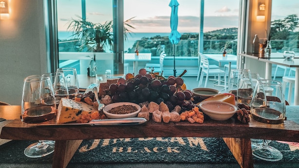 A table with a charcuterie board, glasses, and a view of the outdoors. - Waiheke Island Resort (Waiheke Island)
