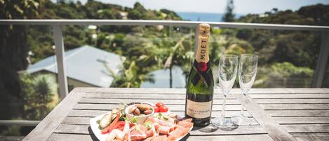 A wooden table with a bottle of Moët & Chandon champagne, two glasses, and a plate of food on a balcony overlooking a scenic view.