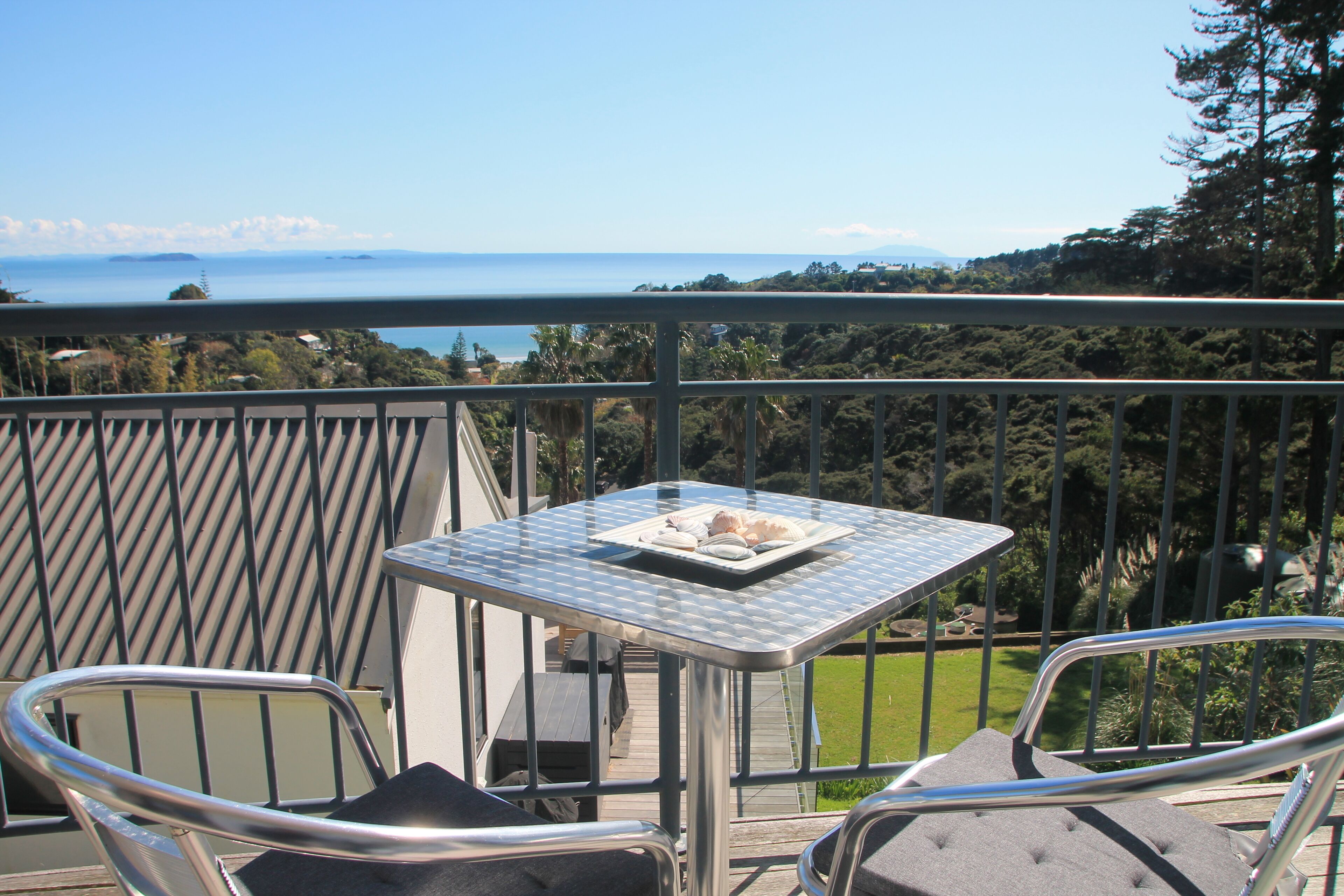 En balkon med et bord og stole, der udover et smukt udsigtspunkt med hav og grønt.