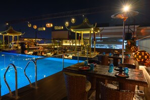 A poolside area with a dining setup, including wicker chairs and tables, and a pool with a metal railing. - Maharaja Regency (Ludhiana)