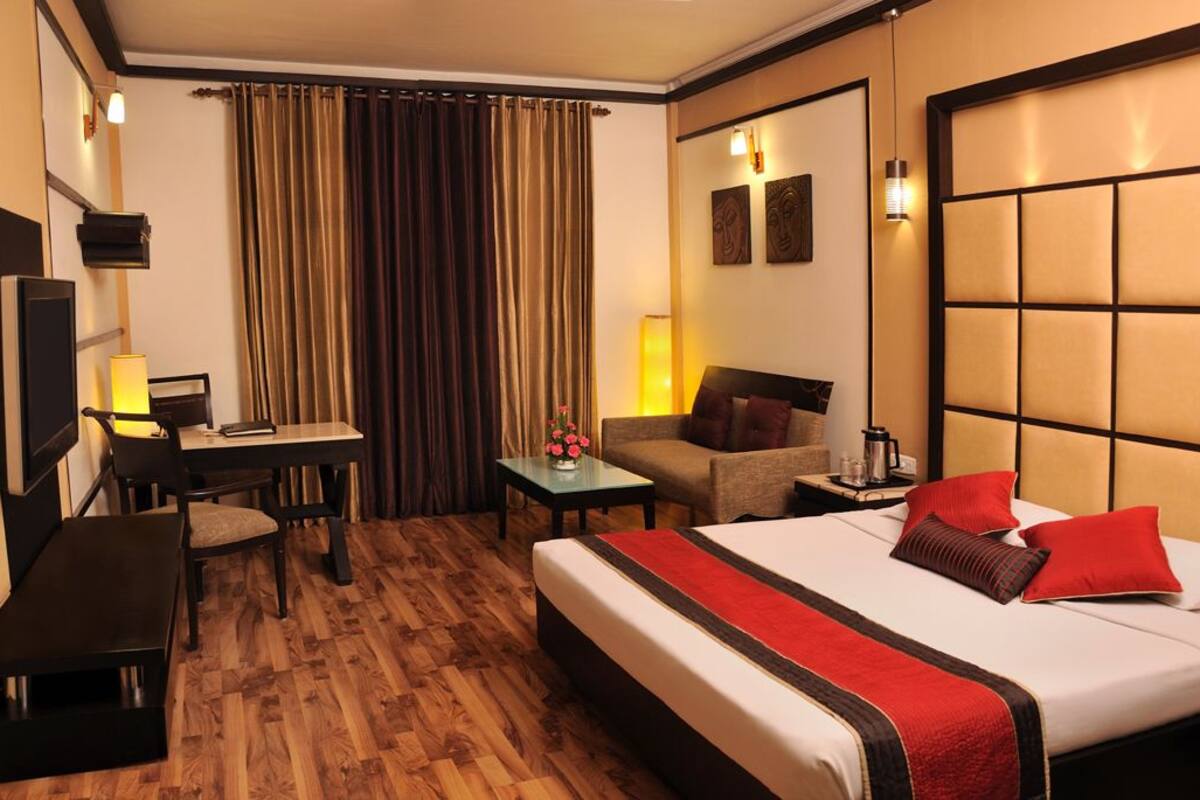 A hotel room with a large bed, a desk, a chair, a small table with a vase of flowers, and a sofa.