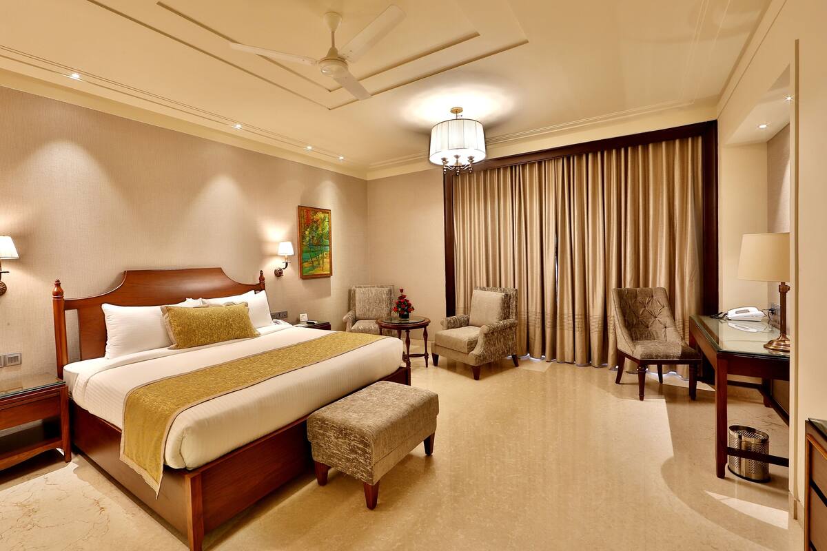A hotel room with a large bed, two chairs, a desk, a lamp, and a ceiling fan.