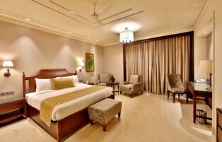 A hotel room with a large bed, two chairs, a desk, a lamp, and a ceiling fan.
