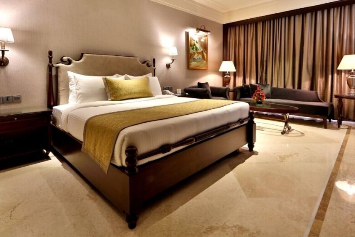 A hotel room with a large bed, a sofa, a coffee table, and two lamps.