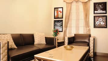 Una sala de estar con un sofá, un sillón y una mesita de centro. Hay cuadros enmarcados en la pared y una ventana con cortinas.
