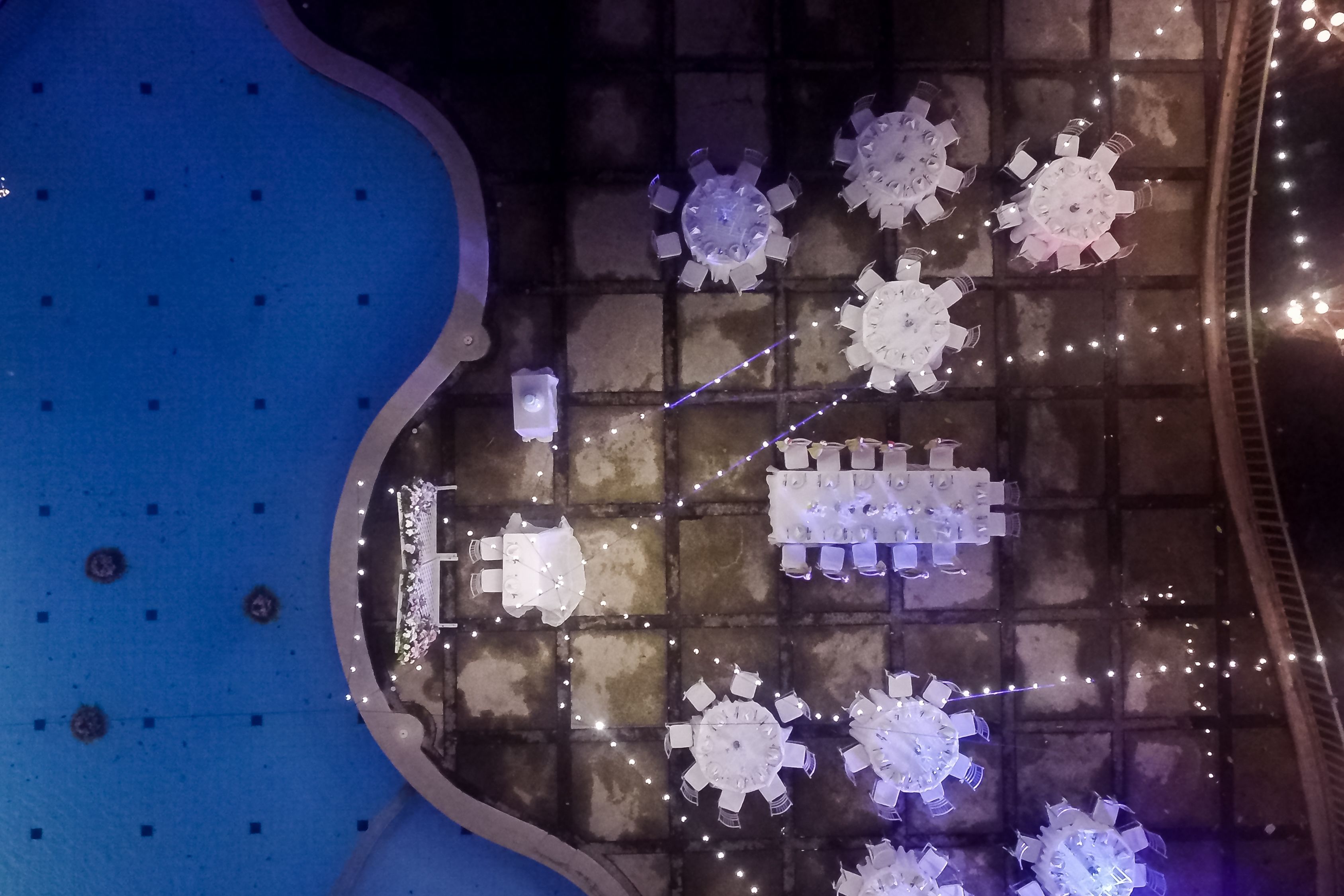 A pool area with multiple seating arrangements and a central table, surrounded by decorative lights.