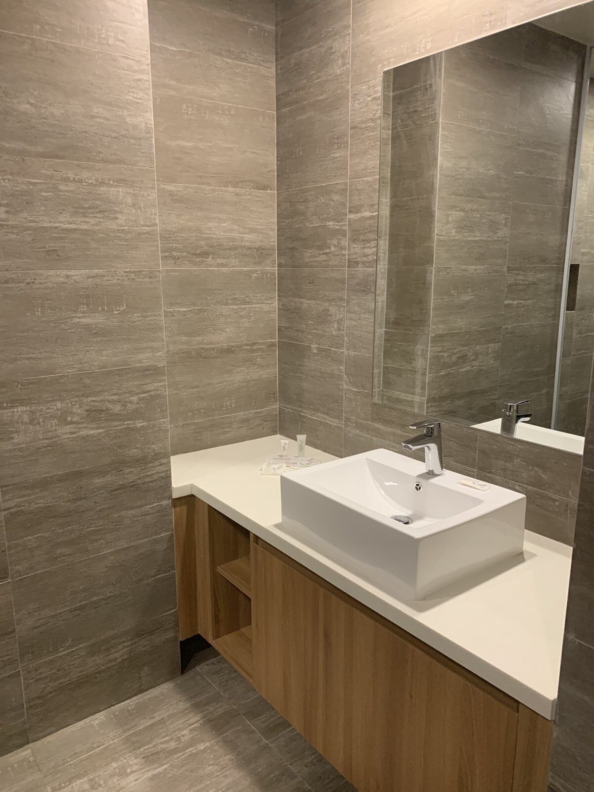 A modern bathroom with a rectangular sink, a mirror, and wooden cabinetry.
