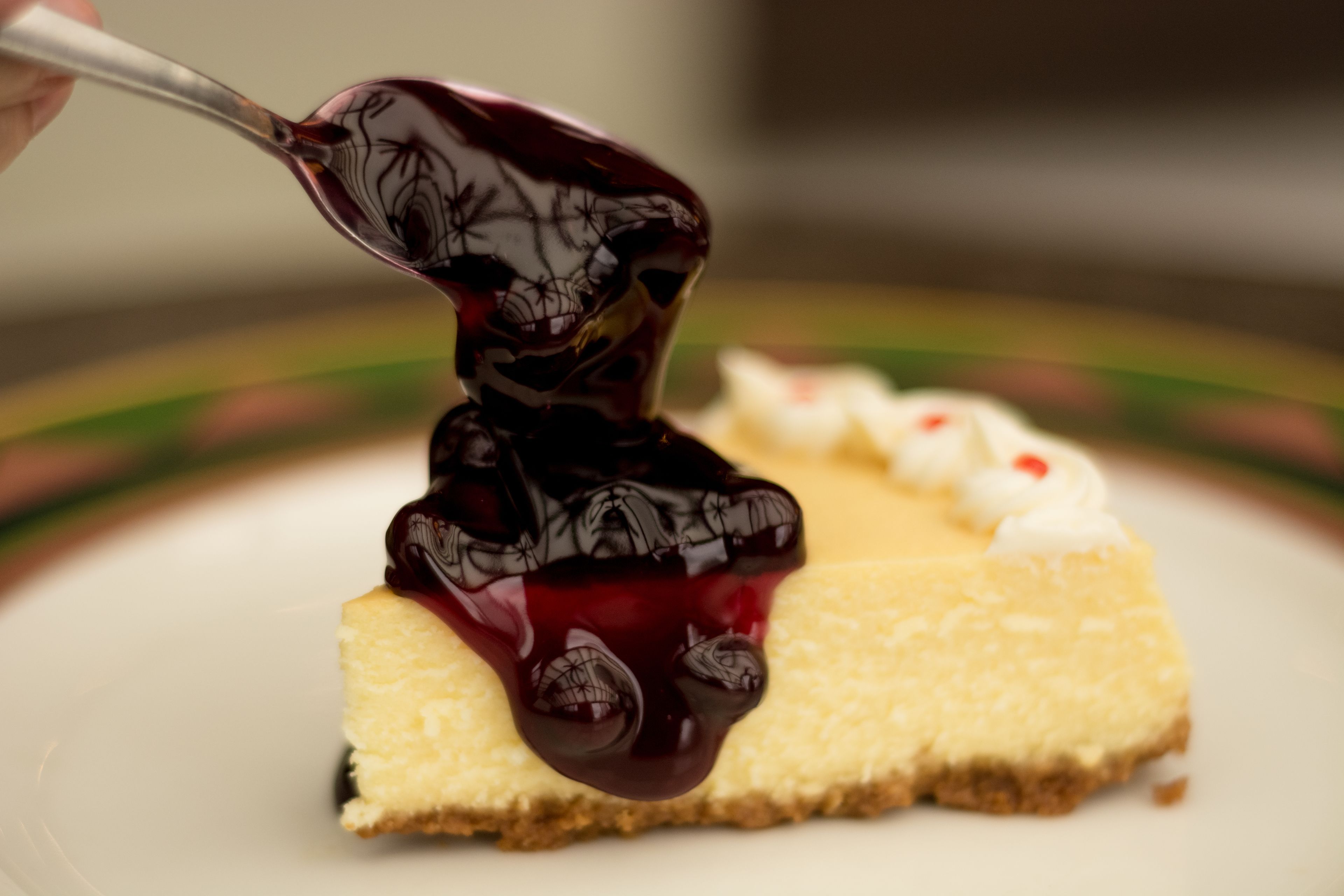 En bit cheesecake med en mörk bärsås, serverad på en vit tallrik.