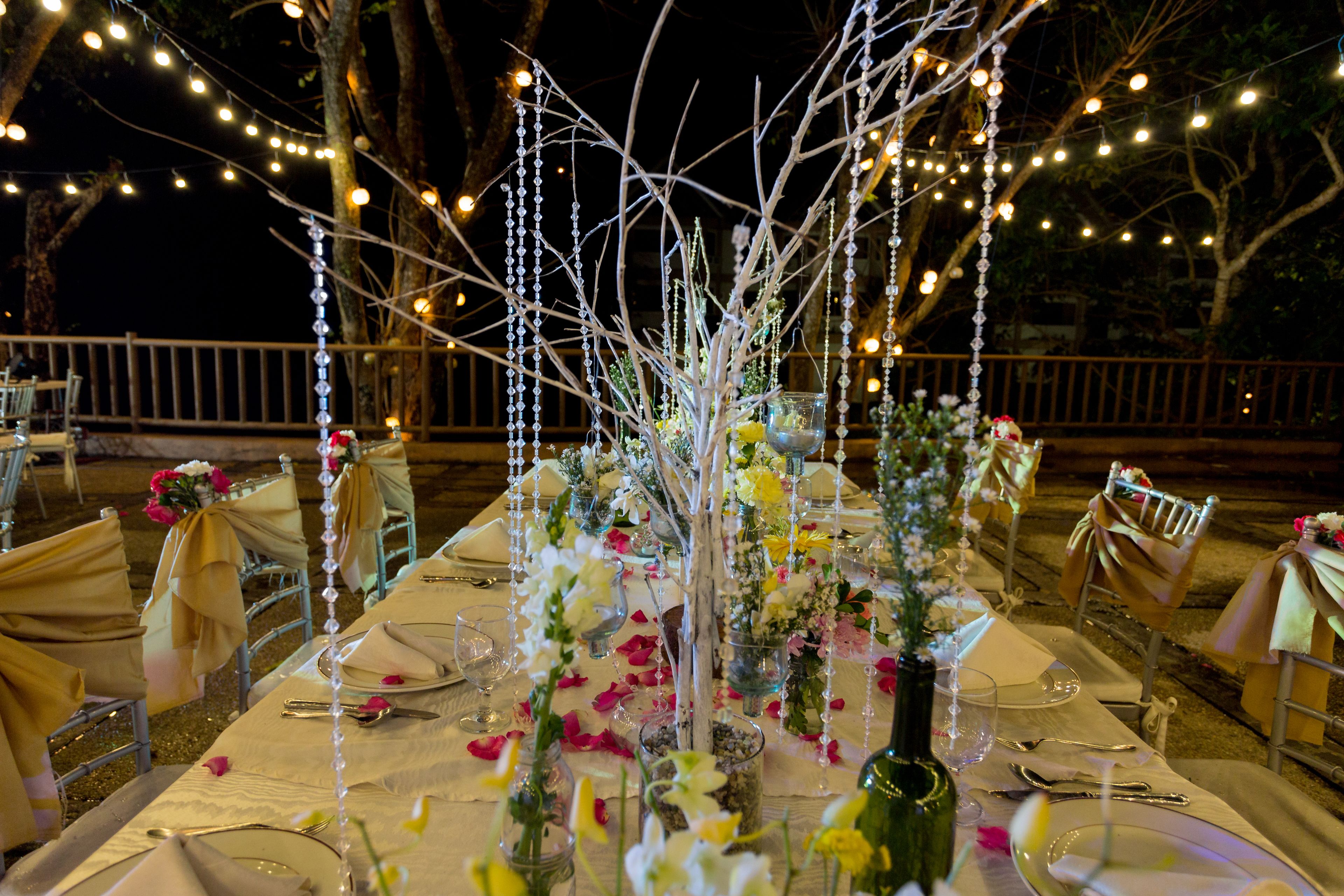 Una mesa lista para un evento al aire libre elegante, con luces de cuerda y centros de mesa florales.