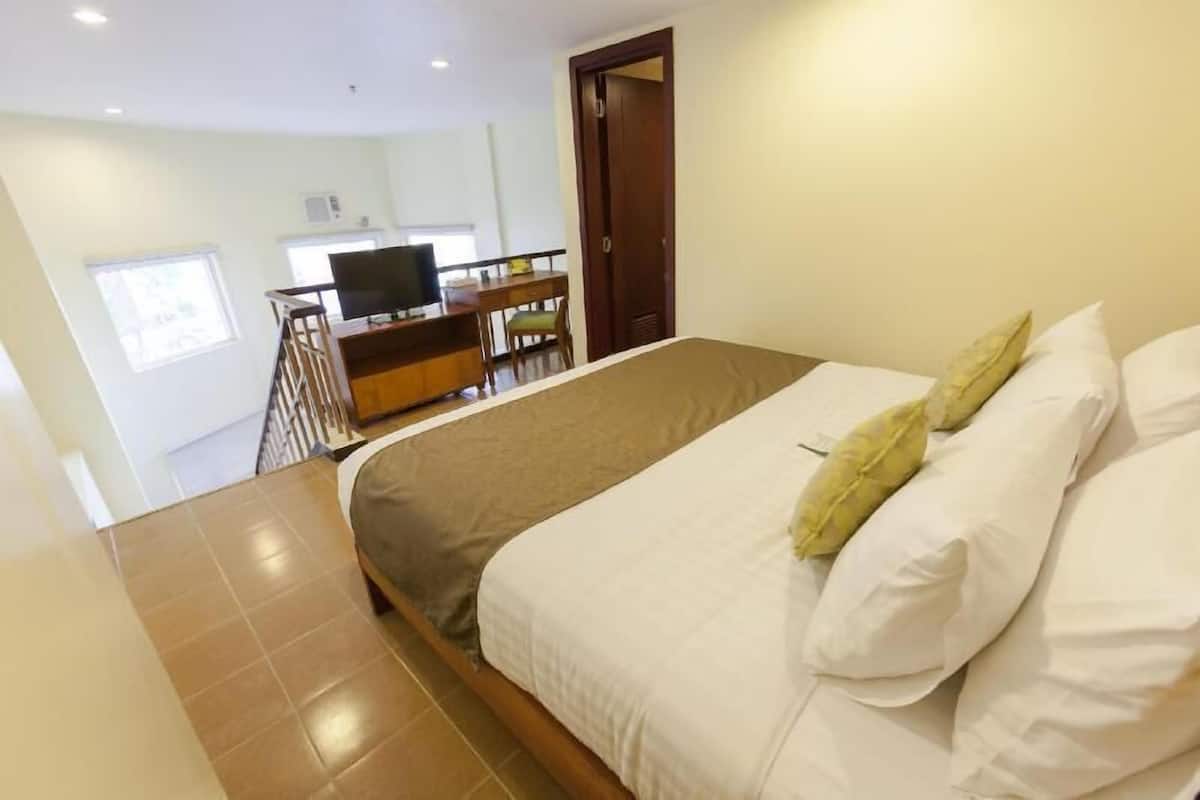 A hotel room with a bed, a desk with a chair, a television, and a window.