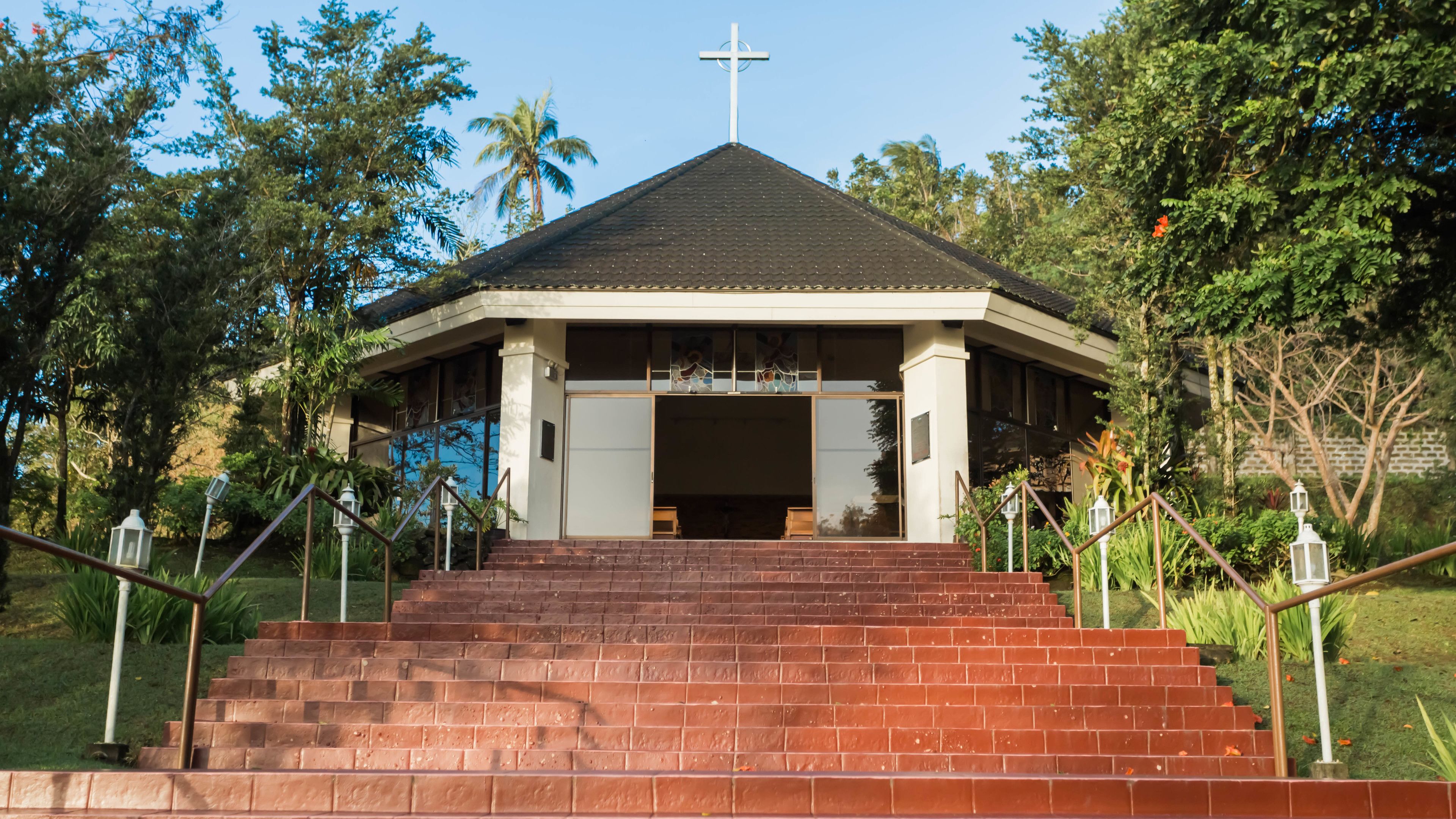 A church with a cross on top, surrounded by trees and a brick staircase leading up to the entrance.