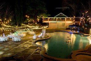 A pool area with a dining setup and a covered seating area, surrounded by trees and string lights. - Canyon Woods Resort Club (Laurel)