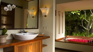 Un baño con un lavamanos grande de color blanco, tocador de madera y un espejo. Se ve una ventana con vistas a la vegetación.