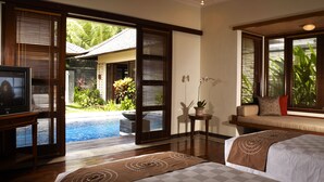 Un dormitorio con una cama grande, televisión, sofá y vista a una piscina.