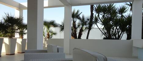 A modern outdoor lounge area with white wicker furniture and potted plants.