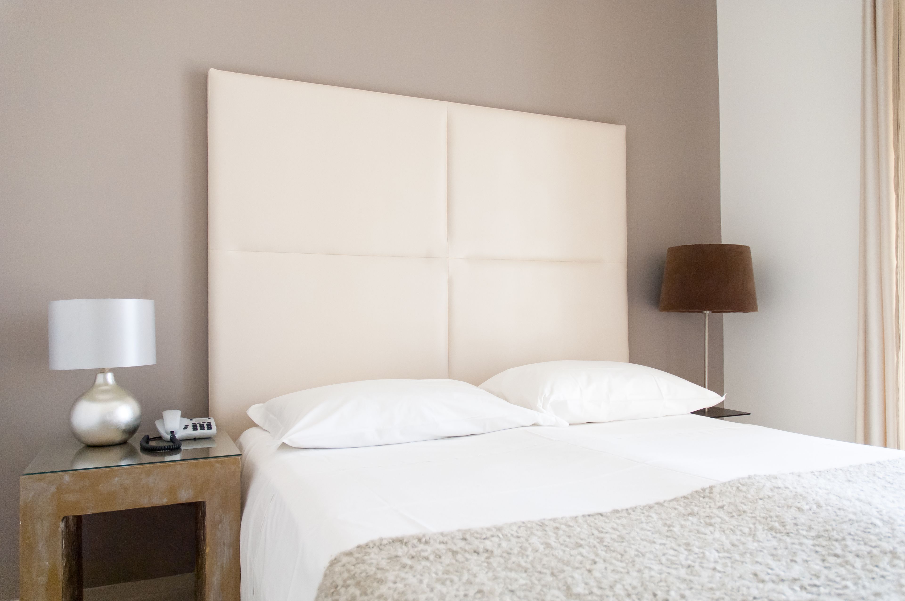 A neatly made bed with white linens, a bedside table with a lamp, and a phone.