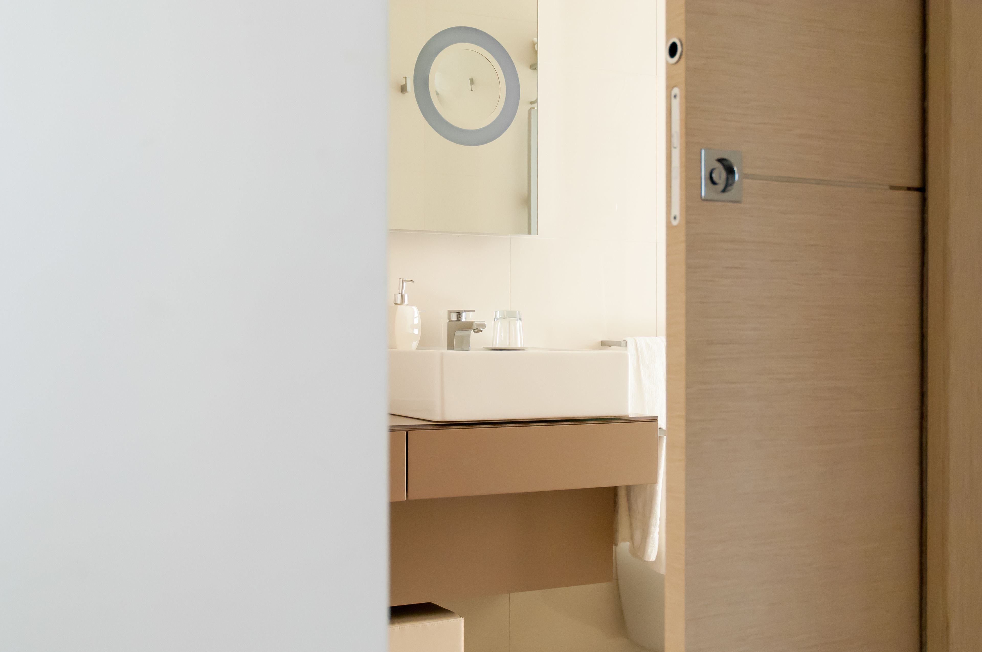 A bathroom with a wooden door, a mirror with a circular frame, a white sink, and a towel hanging on the wall.