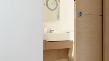 A bathroom with a wooden door, a mirror with a circular frame, a white sink, and a towel hanging on the wall.