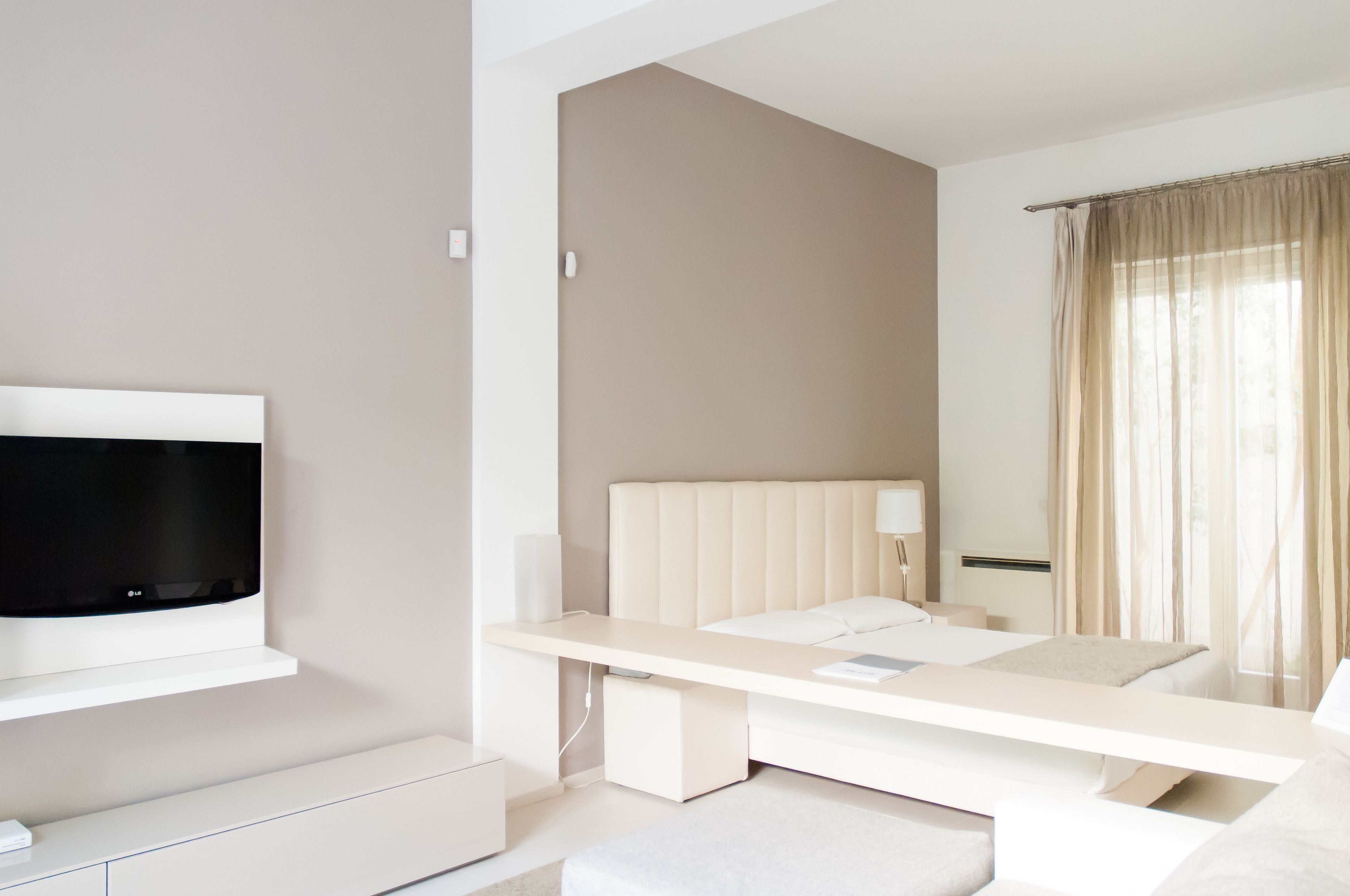 A modern hotel room with a bed, bedside table, TV, and a window with curtains.