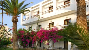 A multi-story building with balconies, surrounded by palm trees and bougainvillea. - Lato Hotel (Agios Nikolaos)
