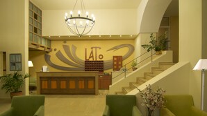 A reception area with a desk, chairs, a staircase, and a chandelier. - Lato Hotel (Agios Nikolaos)