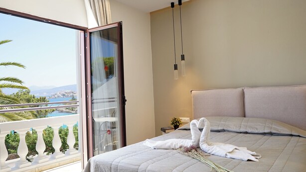 A hotel room with a bed, a balcony with a view, and a window with a plant decoration. - Lato Hotel (Agios Nikolaos)
