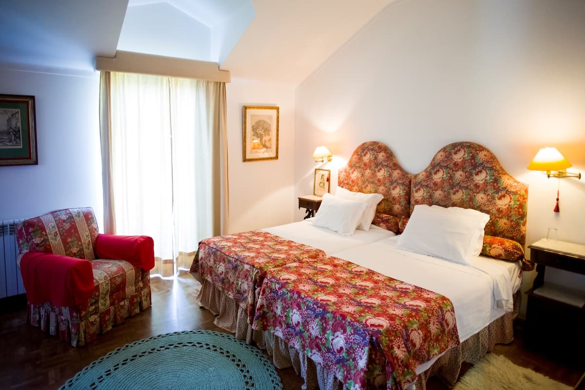 A bedroom with a large bed, two nightstands, a chair, and a window with curtains.