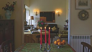 Un coin repas avec une table dressée pour quatre personnes, agrémenté d’un chandelier avec des bougies allumées, d’un bol rempli d’oranges et d’un arrangement floral.