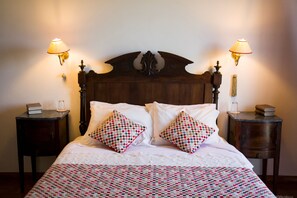 A neatly made bed with patterned pillows, two bedside tables with books and candles, and wall-mounted lamps. - Casa do Castelo (Peniche)