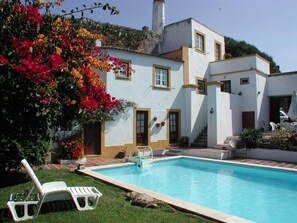A pool area with a white building, a chair, and a potted plant. - Casa do Castelo (Peniche)