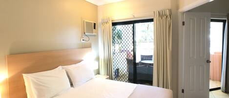 A hotel room with a bed, a nightstand, a ceiling fan, a window with curtains, and a door leading to a balcony.
