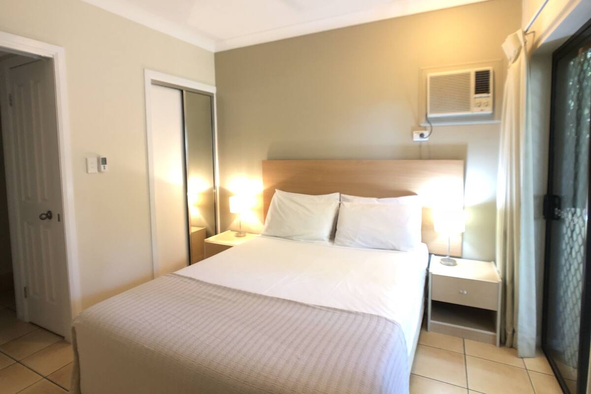 Una habitación de hotel con cama, mesitas de noche, ventilador de techo y aire acondicionado, además de una puerta.