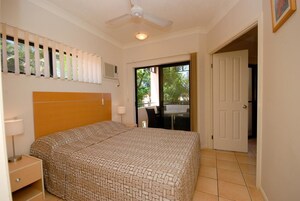 Un dormitorio con cama, mesita de noche, lámpara, ventilador de techo y vistas al exterior a través de una puerta.