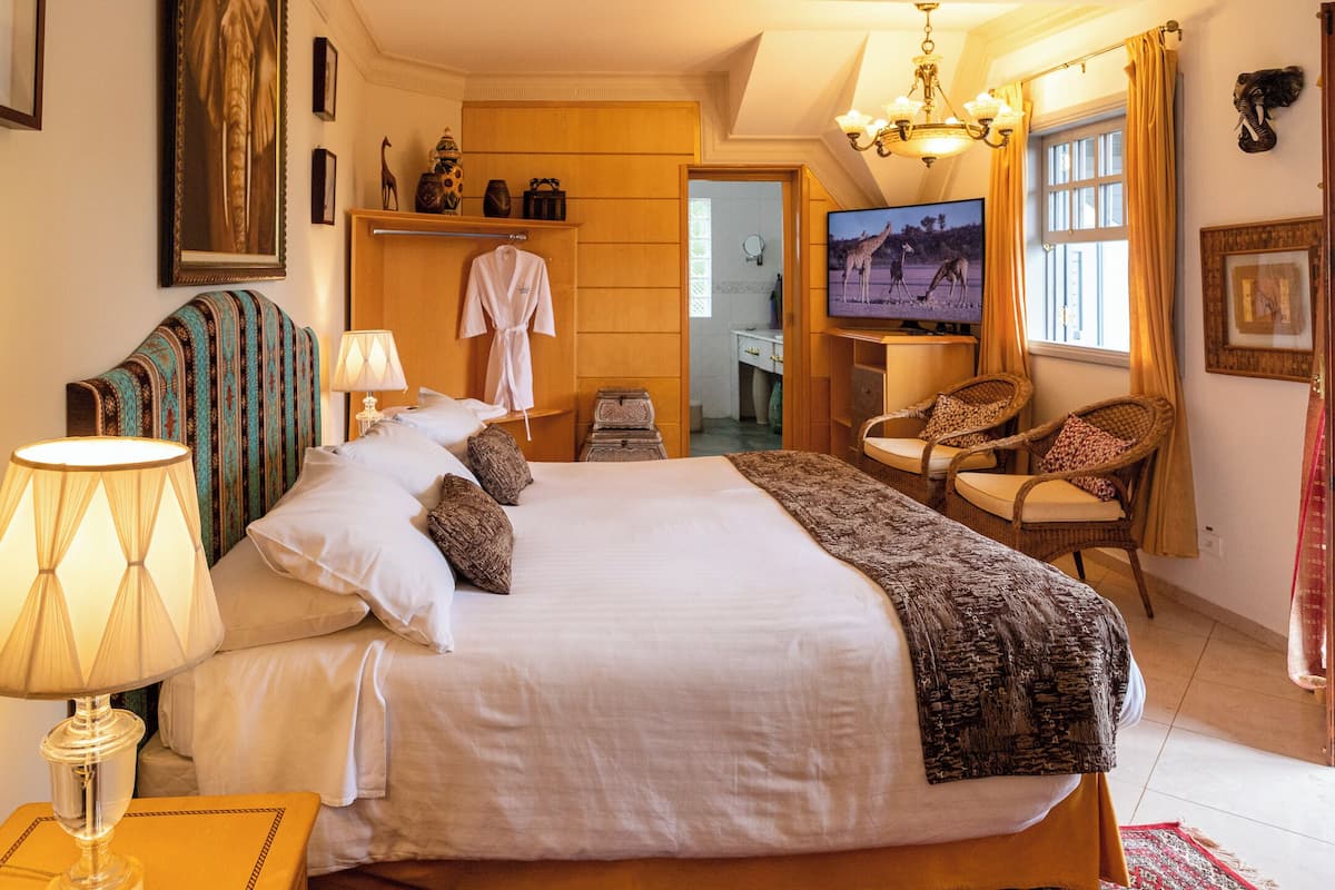 Ein geräumiges Schlafzimmer mit einem großen Bett, einem Fernseher, einer Sitzecke mit Sesseln und einem durchgegangene Tür erkennbaren Badezimmer.