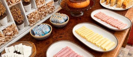Buffet com diversos alimentos, incluindo massa, presunto, queijo e frutas.