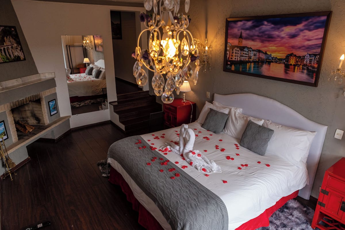 Ein stilvoll eingerichtetes Schlafzimmer mit einem großen Bett, einer Kristallleuchter, einem Stadtbildgemälde und einer Treppe, die in eine weitere Ebene führt.