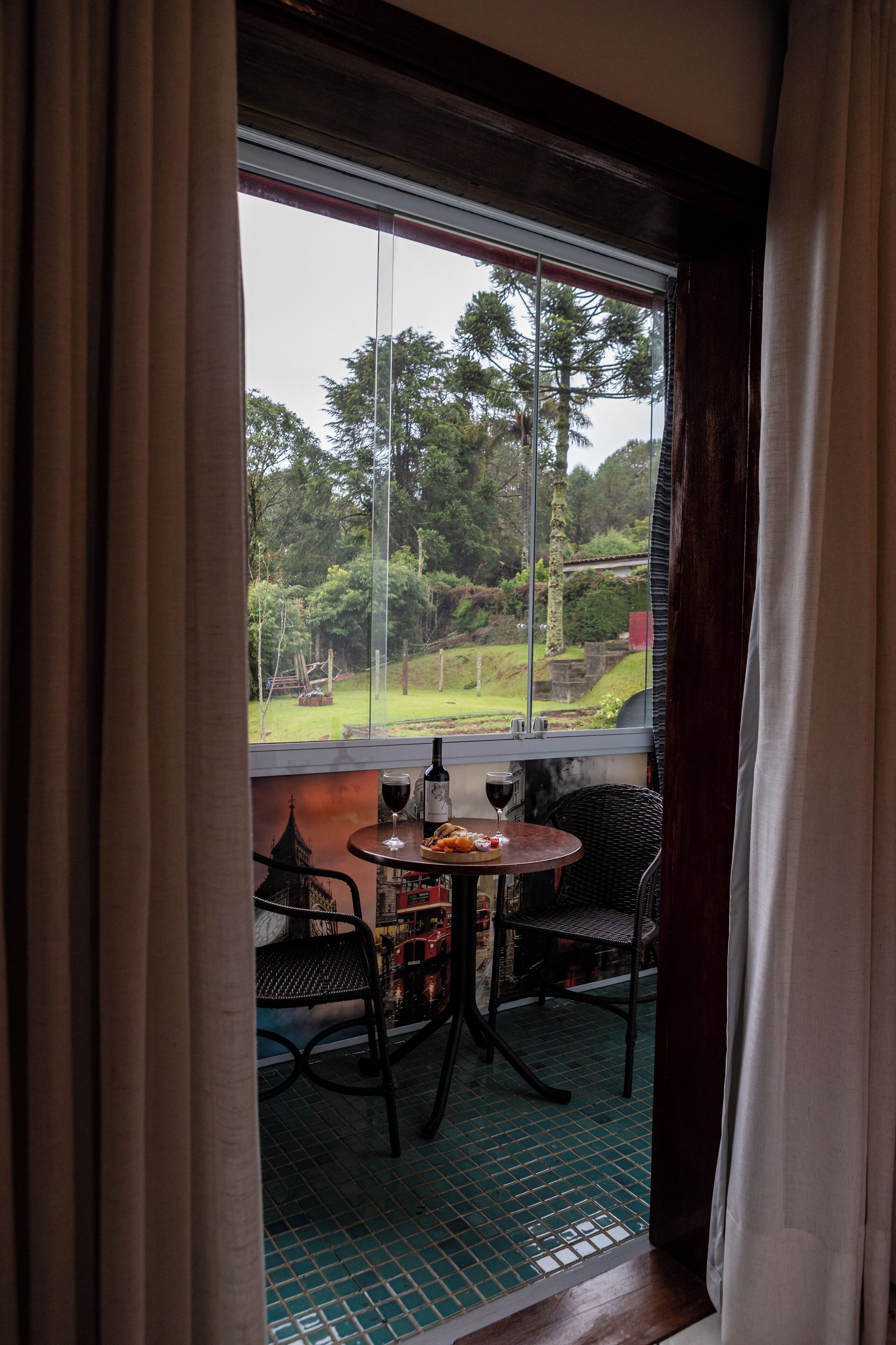 Ein Zimmer mit großem Fenster, einem Tisch mit Stühlen und einer Weinflasche.
