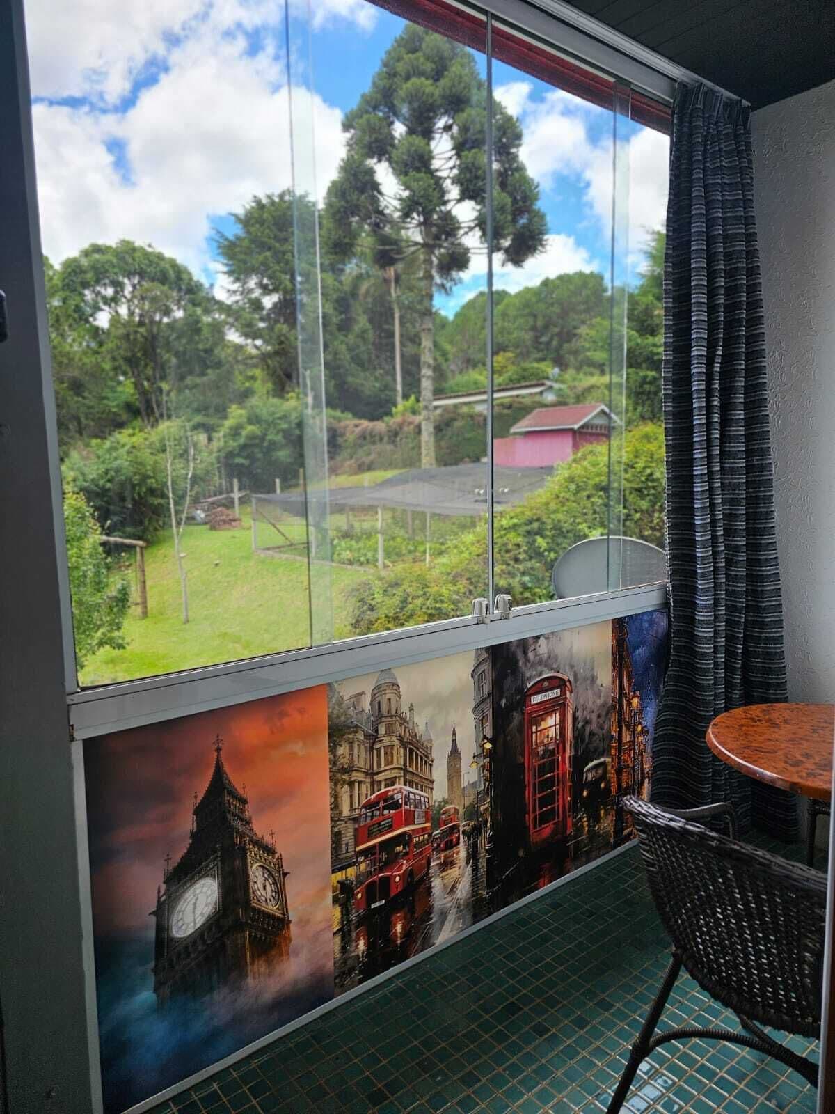 A room with a large window offering a view of a garden and trees. There is a mural of London landmarks on the wall below the window.