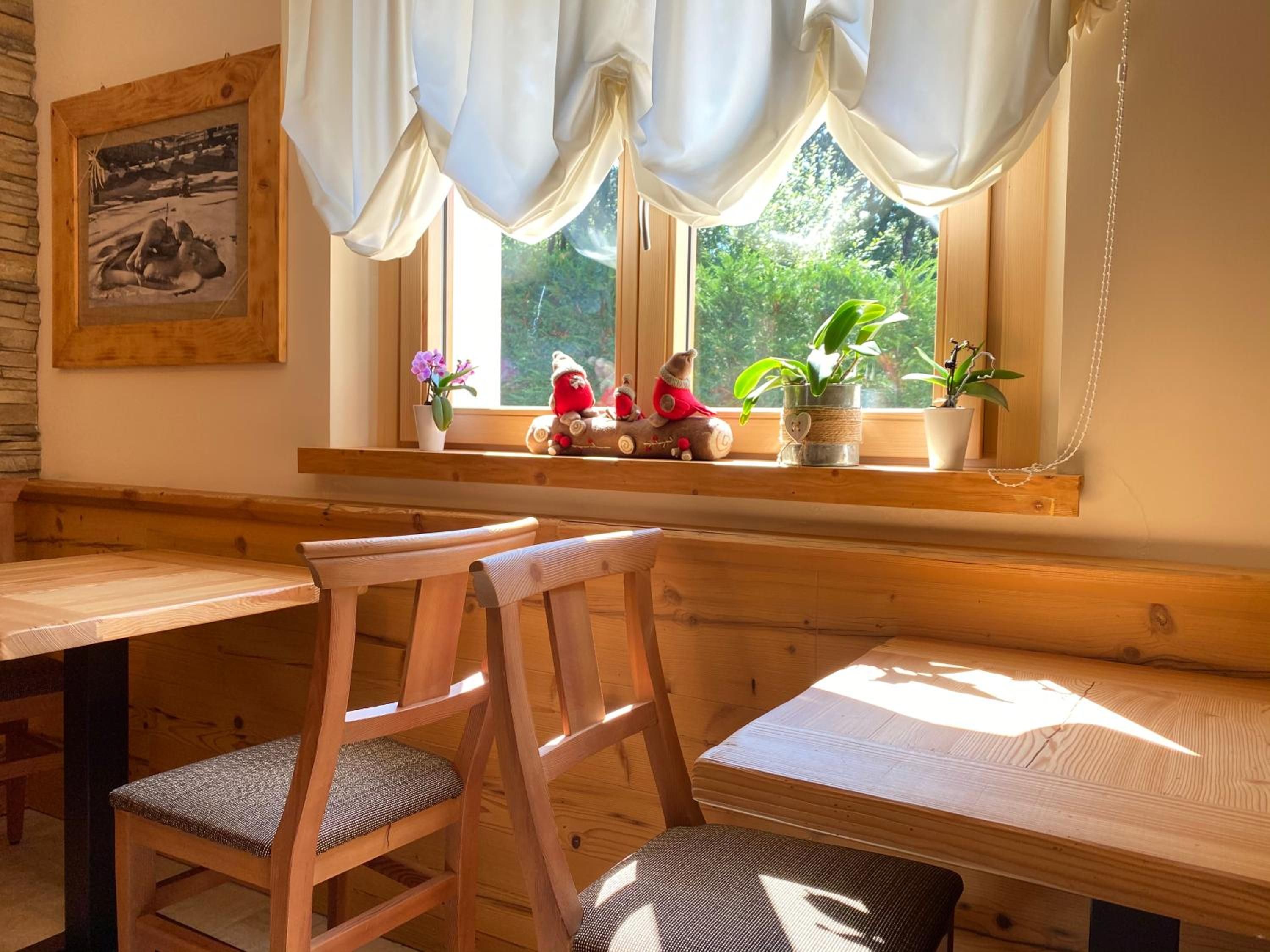 Un banco y una mesa de madera en una habitación con ventana, un cuadro en la pared y plantas en macetas en el alféizar.