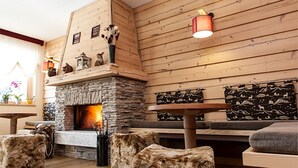 A cozy room with a stone fireplace, wooden walls, and a bench with patterned cushions. - Boutique Hotel Il Riccio (Roccaraso)