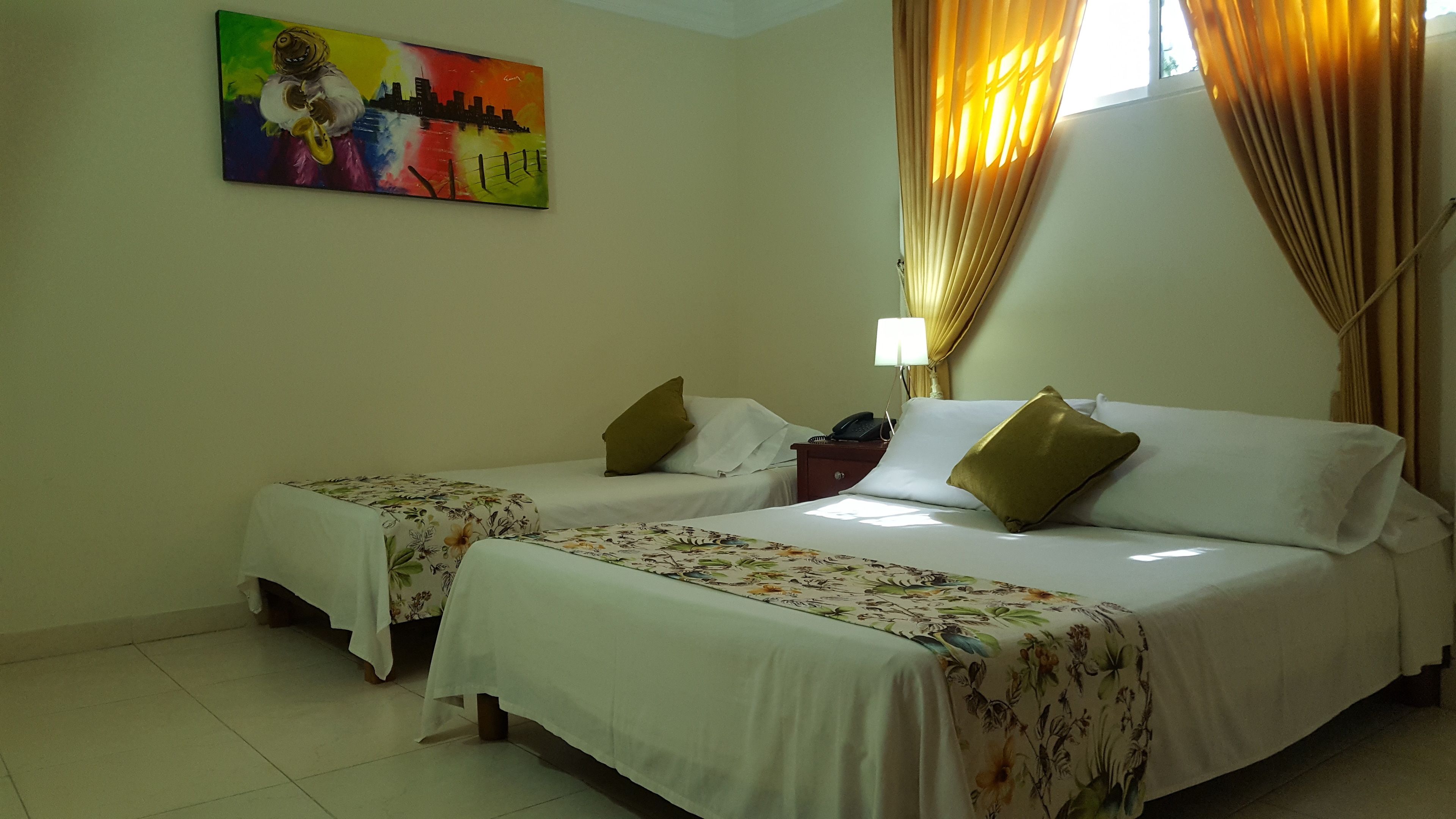A hotel room with two beds, floral bedspreads, a painting on the wall, a nightstand with a lamp, and curtains.