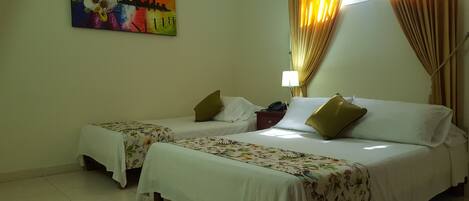 A hotel room with two beds, floral bedspreads, a painting on the wall, a nightstand with a lamp, and curtains.