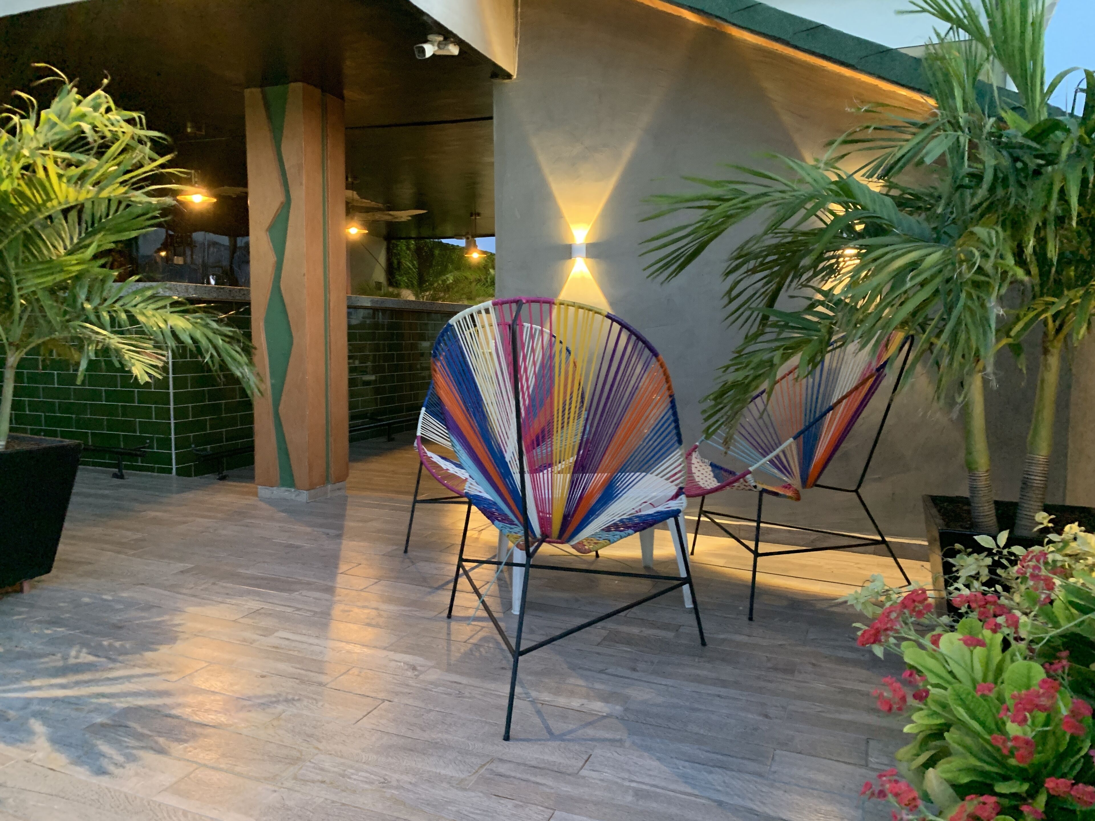 Un espace patio agrémenté de deux chaises colorées en fibres tressées, d’une plante en pot et d’un luminaire fixé au mur.