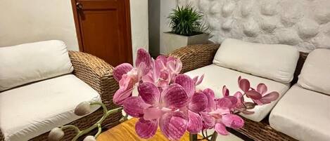 Una habitación con dos sofás blancos, una mesa de centro de madera con una orquídea en maceta y una pared con textura.